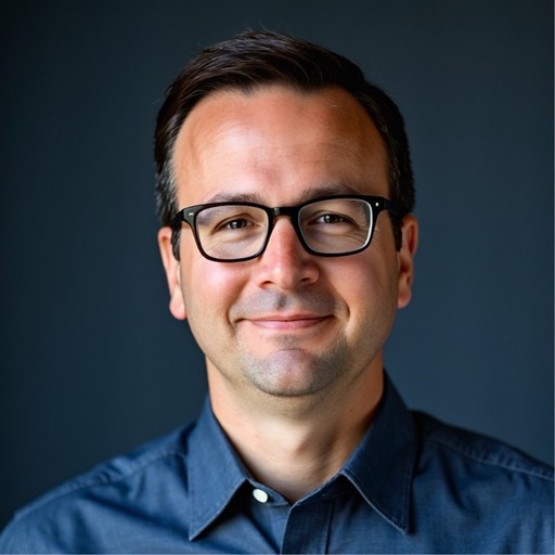 A focused woman with long red hair is seated at a desk, wearing a black blazer and dark blouse. She intently looks at camera, smiling slightly, with an open laptop in front of her. The setting is a warm and serene office setup in the background. Soft daylight filters through, creating a calm atmosphere. The composition captures her in a frontal profile with a clear emphasis on her concentration and the serene indoor setting.