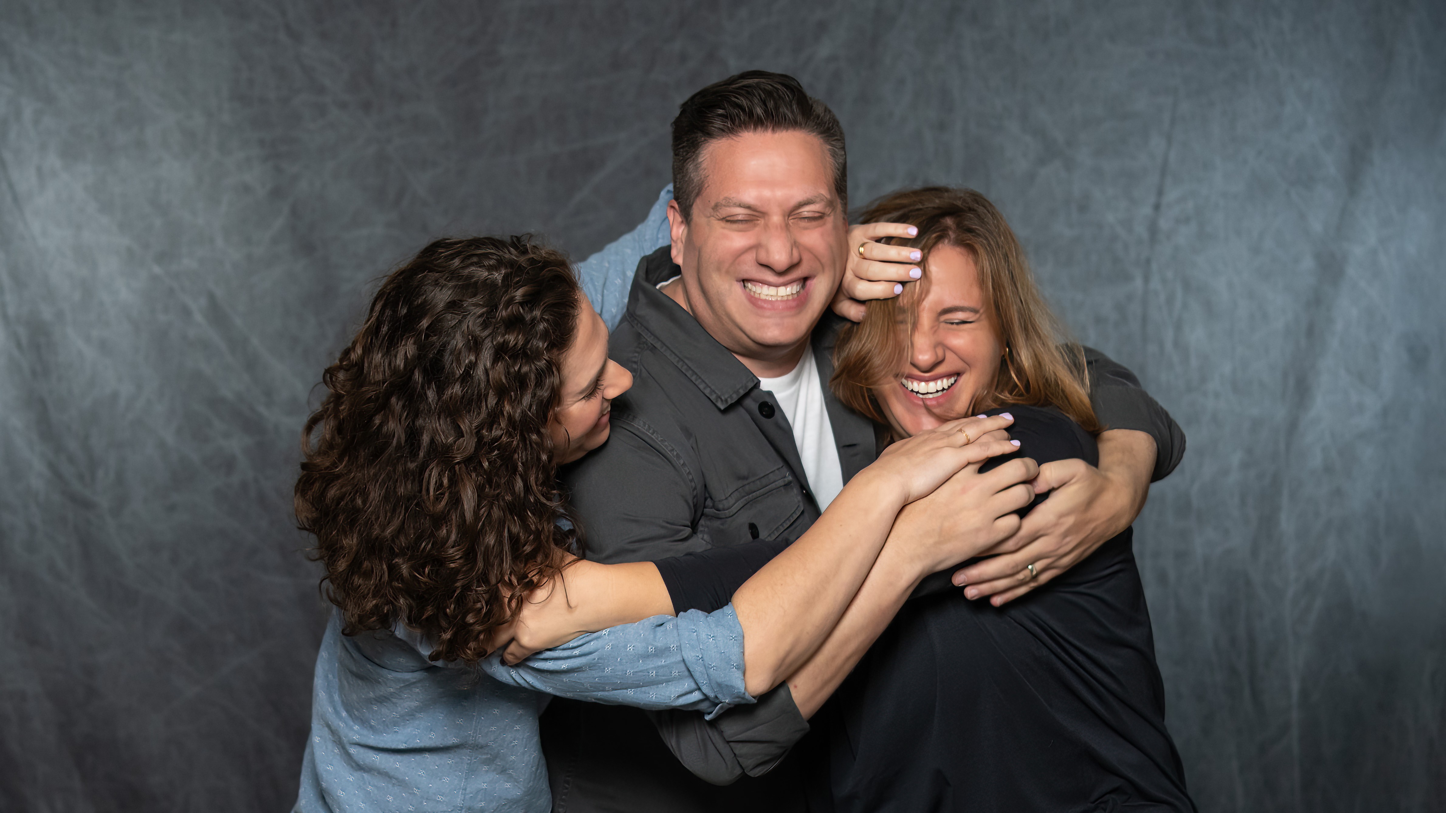 Portrait of the Korman siblings laughing and embracing each other in a playful group hug.