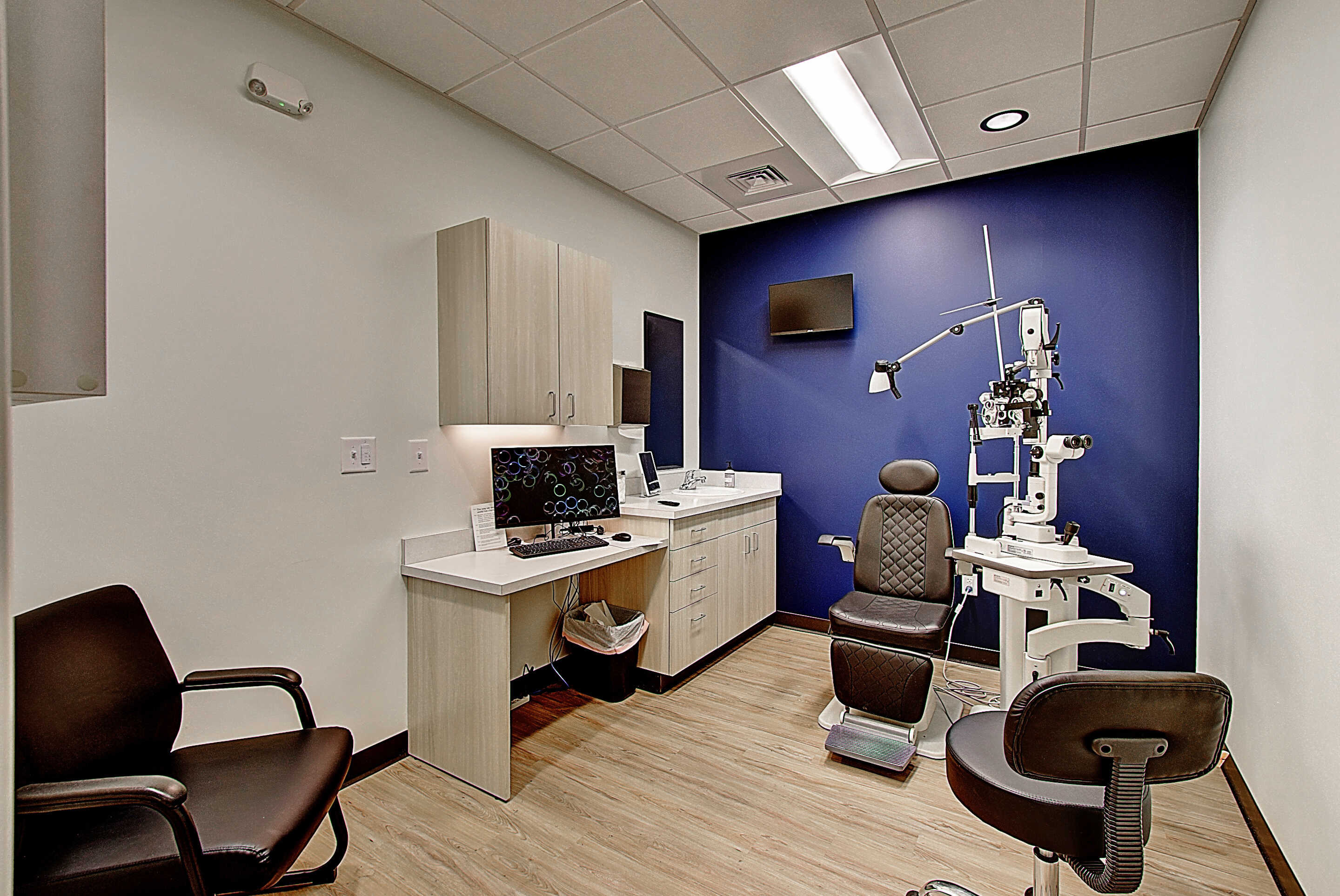 A modern medical examination room featuring an eye exam chair, diagnostic equipment, and a clean, minimalist design.