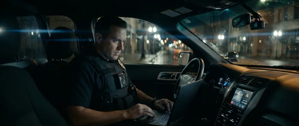 Police officer using a rugged laptop inside a patrol vehicle at night, showing how mobile technology supports daily law enforcement work