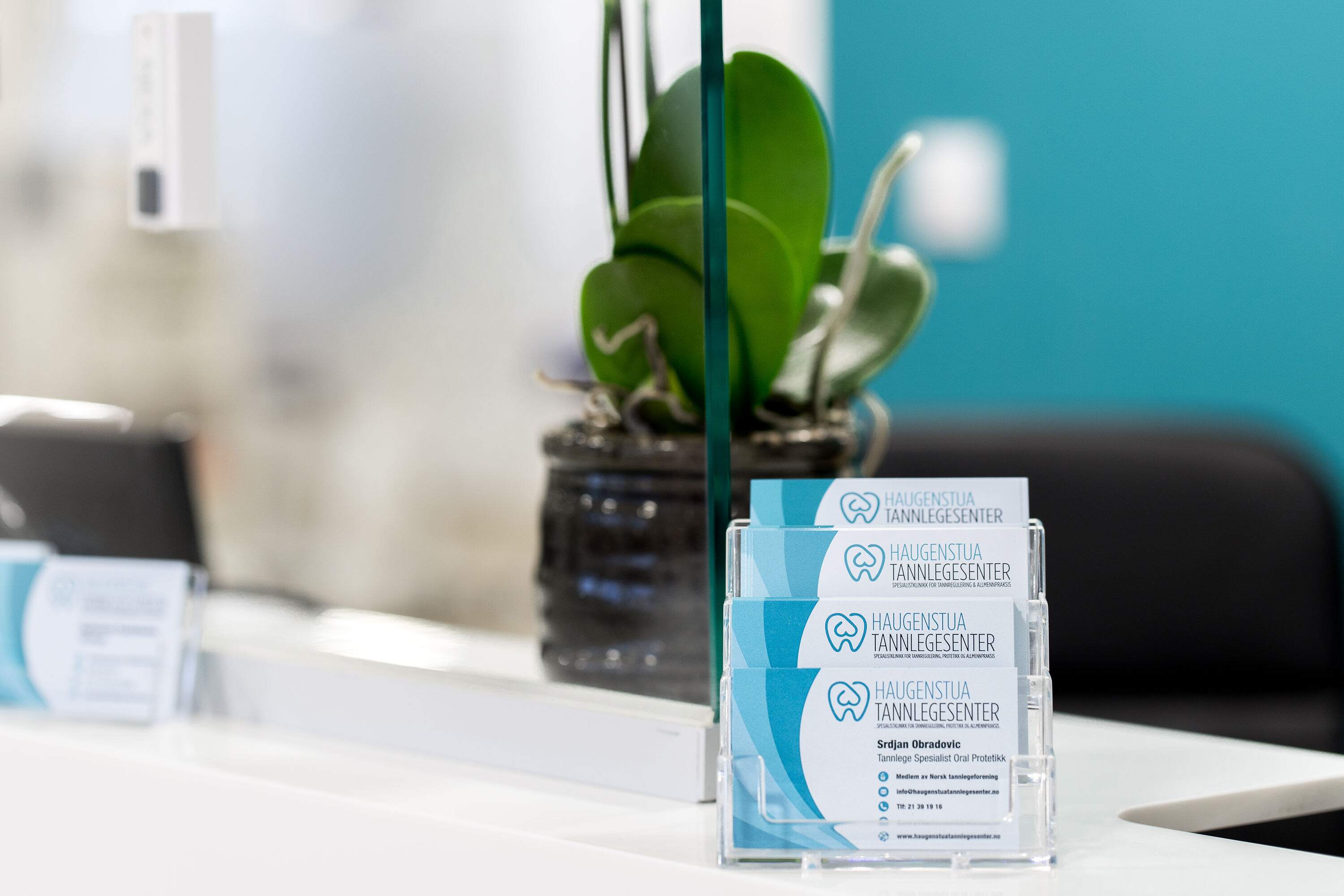 Visittkort fra Haugenstua Tannlegesenter på resepsjonsdisken, som viser profesjonell tannklinikk i Oslo med moderne tannhelsetjenester.