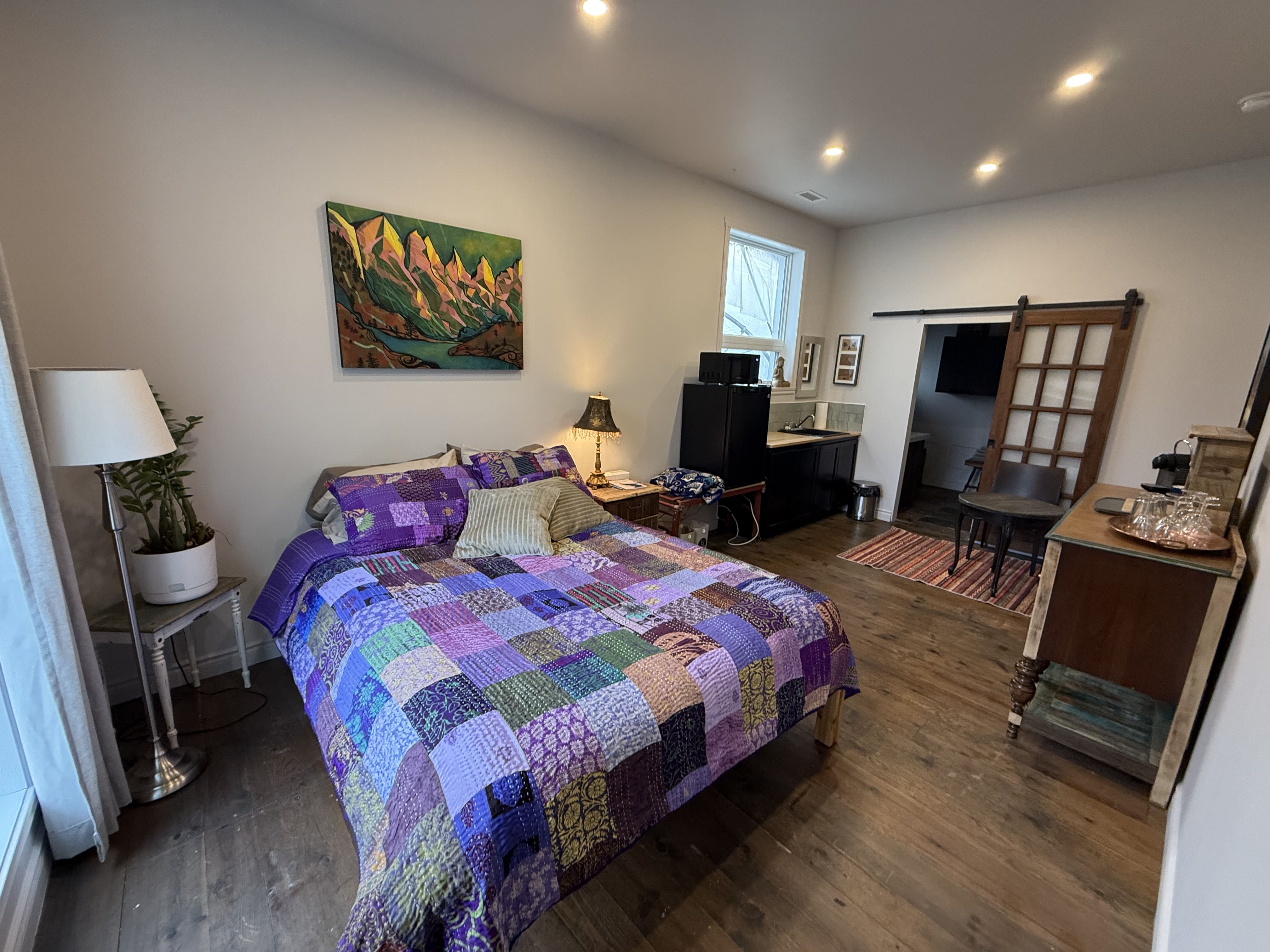 Grand lit recouvert d’une courtepointe patchwork violette et mauve, plancher en bois naturel, statue de Bouddha et porte coulissante en bois.