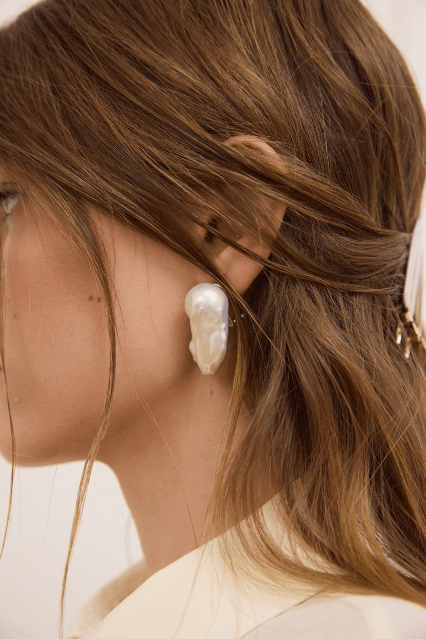 Close-up of a person wearing a pearl earring with a neutral background