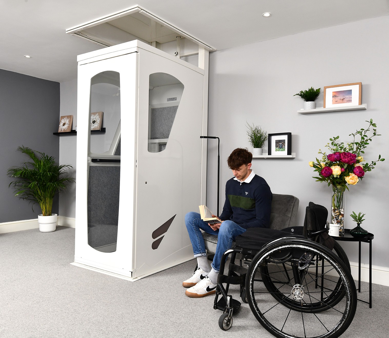 Elevate AVA home lift closed with door shut in a residential living room — wheelchair user seated alongside reading a book