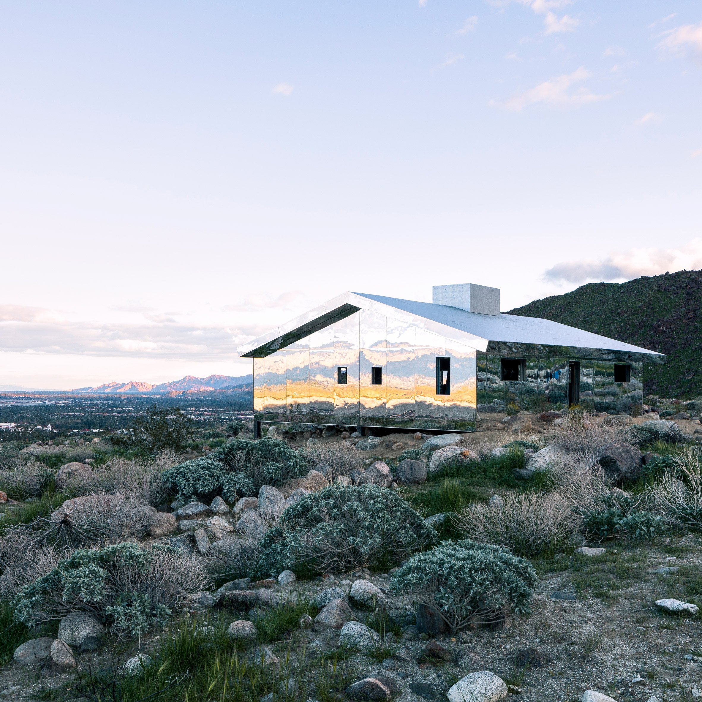 Minimalist white house mirrored in a stil desert, surrounded by wild landscape — calm, architectural, quietly dramatic.