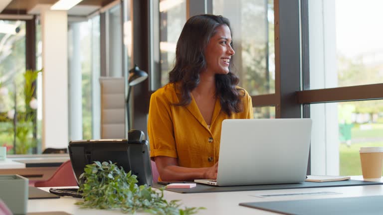 A woman stands in an office, with social media icons emerging from her laptop, symbolizing digital connectivity and engagement.