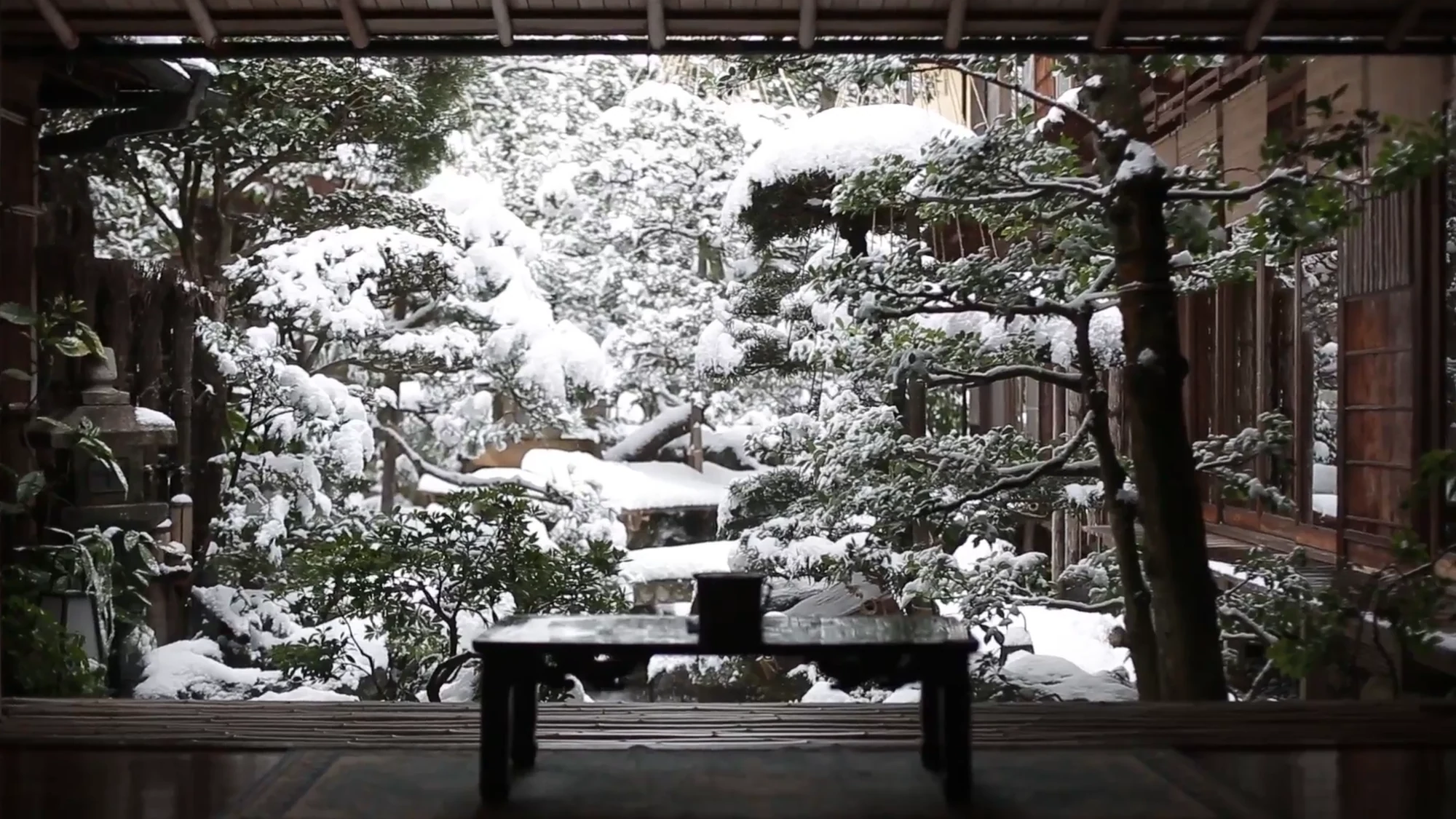 A snow-covered inn garden seen from a tatami room in Kinosaki, low table in the foreground.