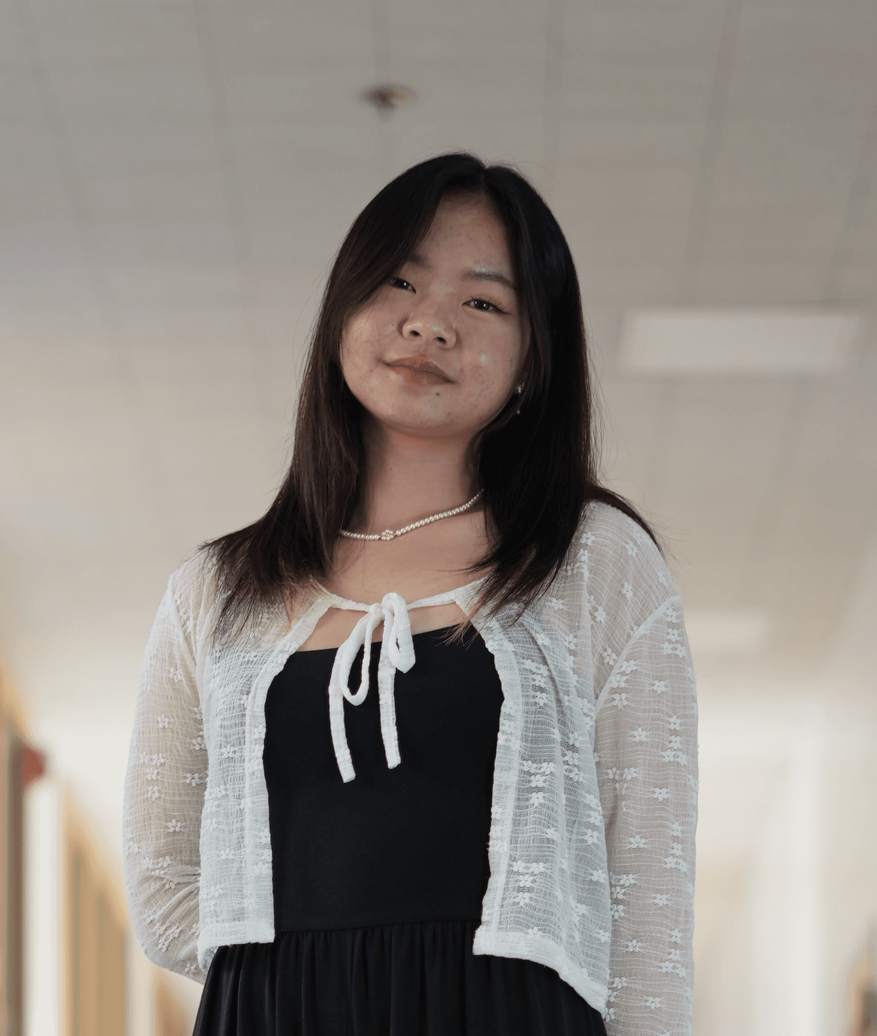 Jess Fong standing in a hallway with a white sweater and black top