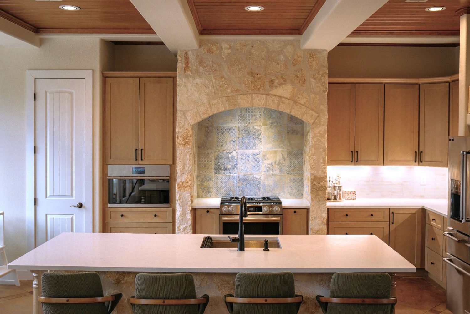 Custom natural oak kitchen with travertine stone backsplash and arched range hood in Austin Texas home