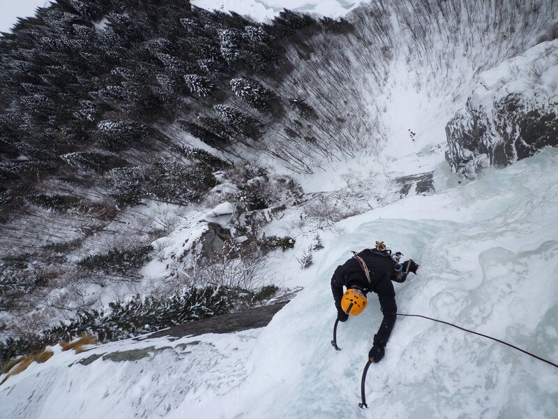 Beginner ice climber learning rope management and positioning on ice during an ice climbing fundamentals clinic course in the Dolomites.