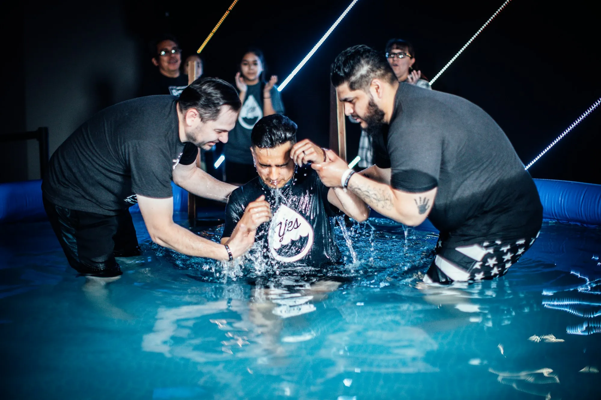 A man being baptized in a pool, surrounded by friends