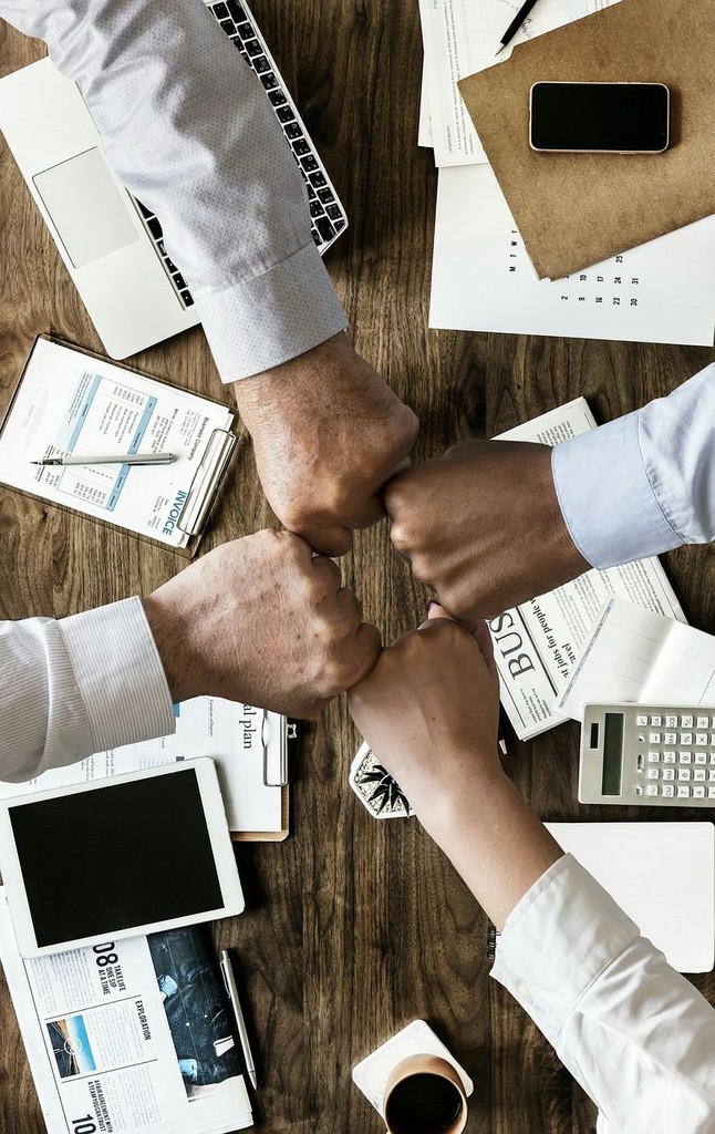 Close-up portrait of a person wearing a gray insulated hooded jacket with the hood up, showing their face framed by the hood against a light background.