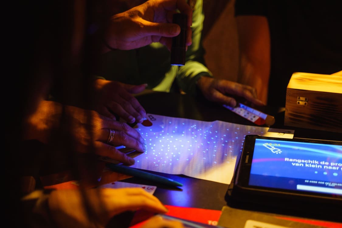 Deelnemers lossen samen een puzzel op met een UV-zaklamp tijdens een interactieve teambuildingactiviteit van The Box Company.