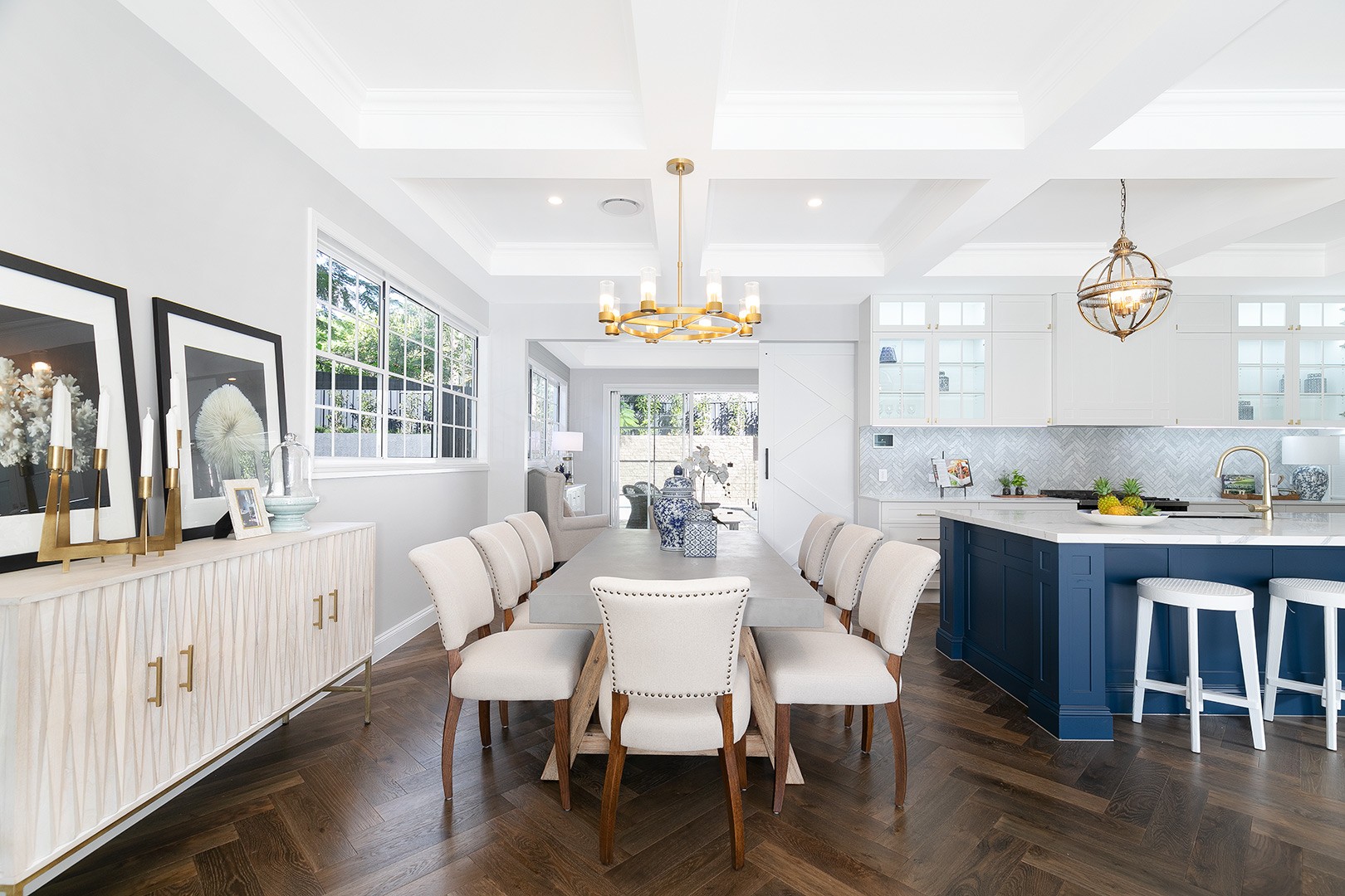 The dining room with a view of the kitchen and a living area with a gold chandelier hanging over the table
