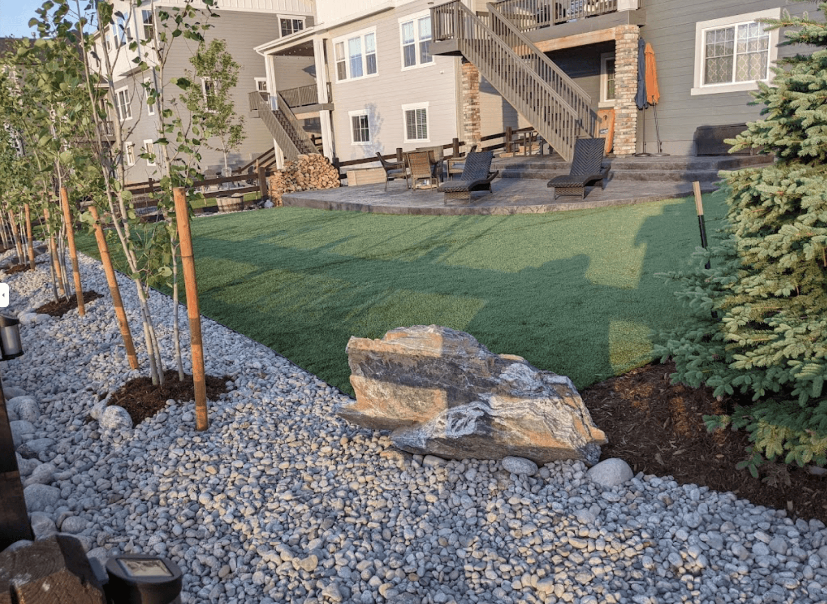 artificial grass installation in the backyard with rocks and pebbles around it, with a green and grey color combination