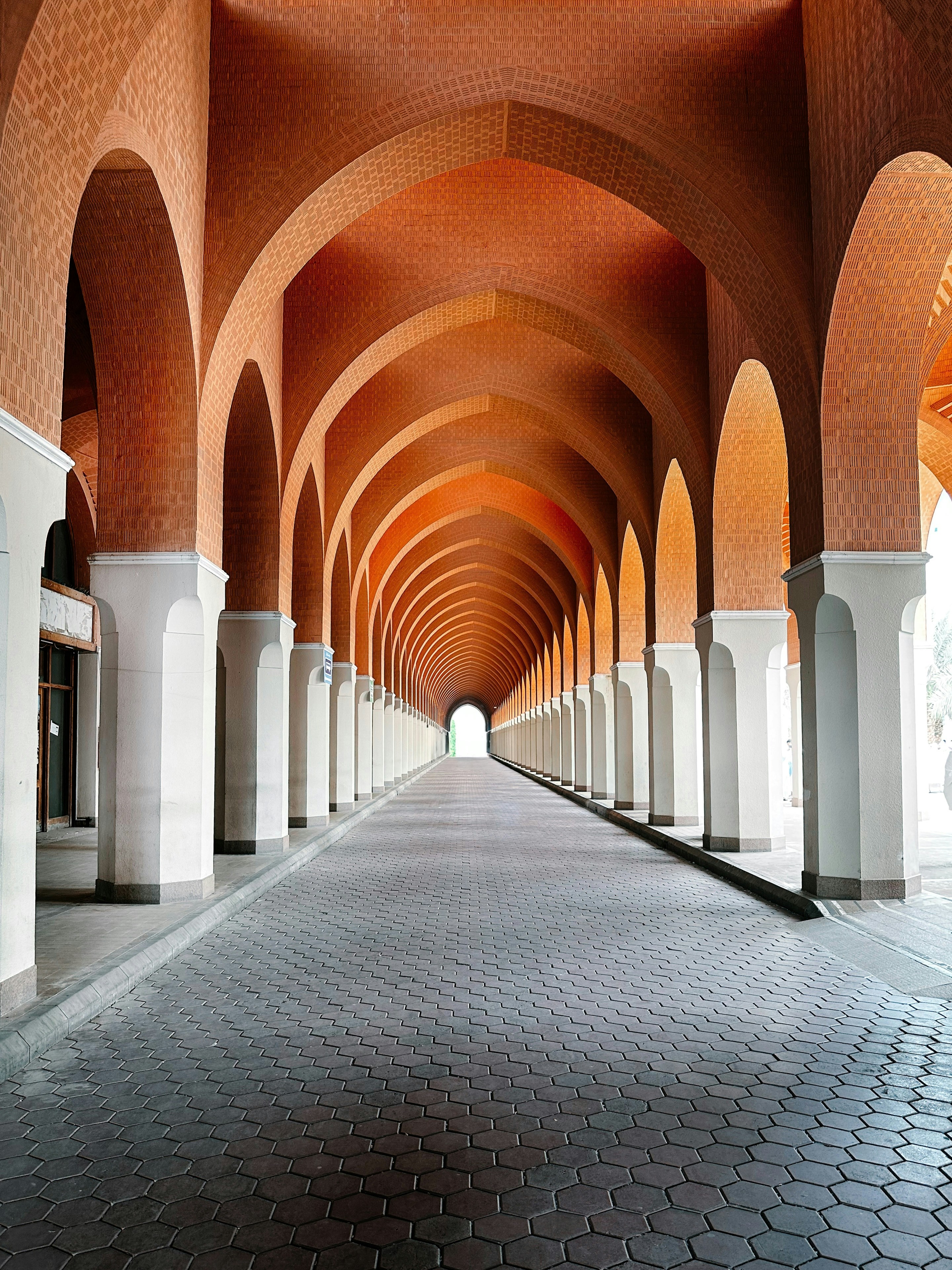 Long arched hallway with white columns and brick ceiling.