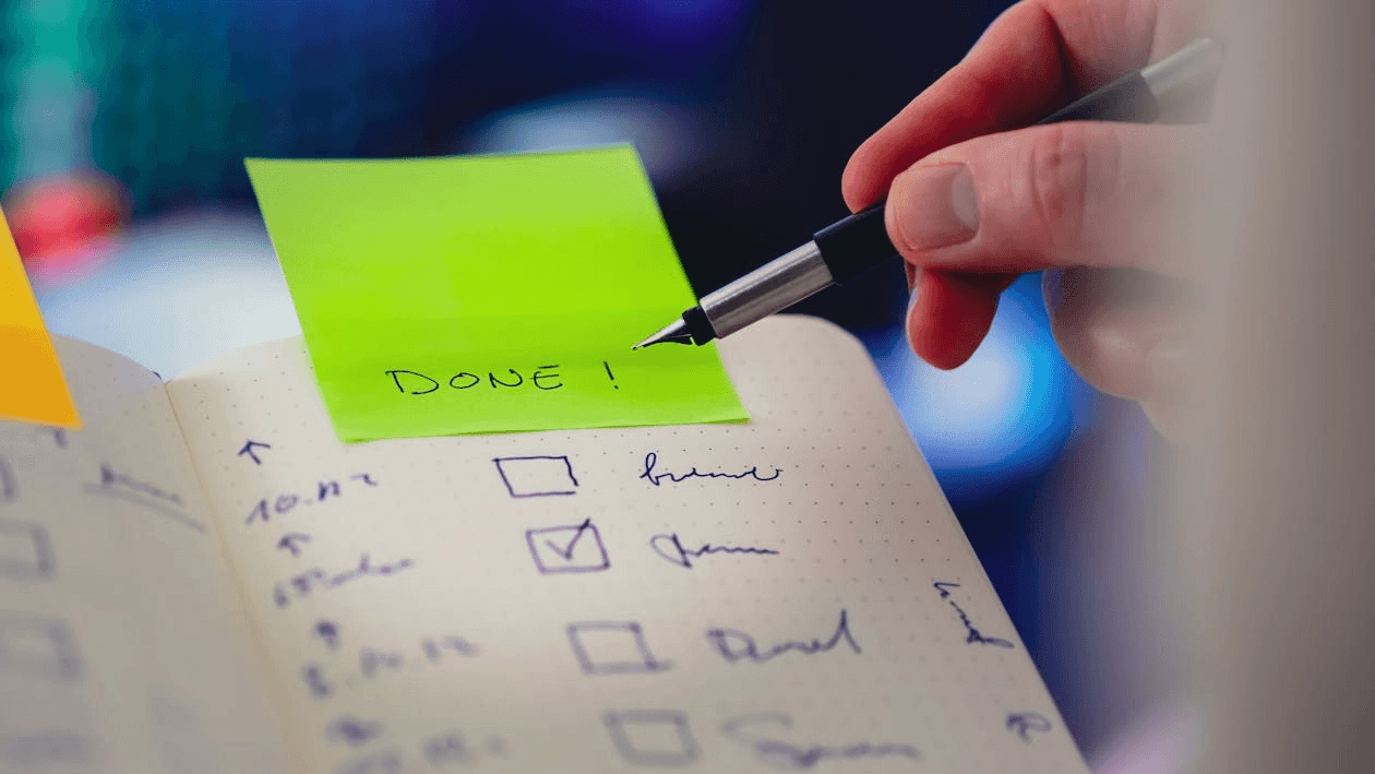 펼쳐진 줄 노트에 볼펜으로 체크리스트 항목을 검토하던 중, 노트 상단에 붙은 연두색 포스트잇에 'DONE!' (완료!)이라고 적고 있는 손의 근접 촬영 사진입니다. 인터넷 티비 가입 전 확인해야할 리스트를 모두 확인했음을 상징합니다.