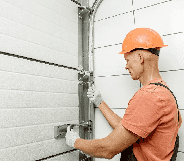 Professional technician in a hard hat performing a garage door installation and hardware adjustment. Close-up of a white sectional door track being secured with industrial tools, showcasing expert maintenance and repair services.