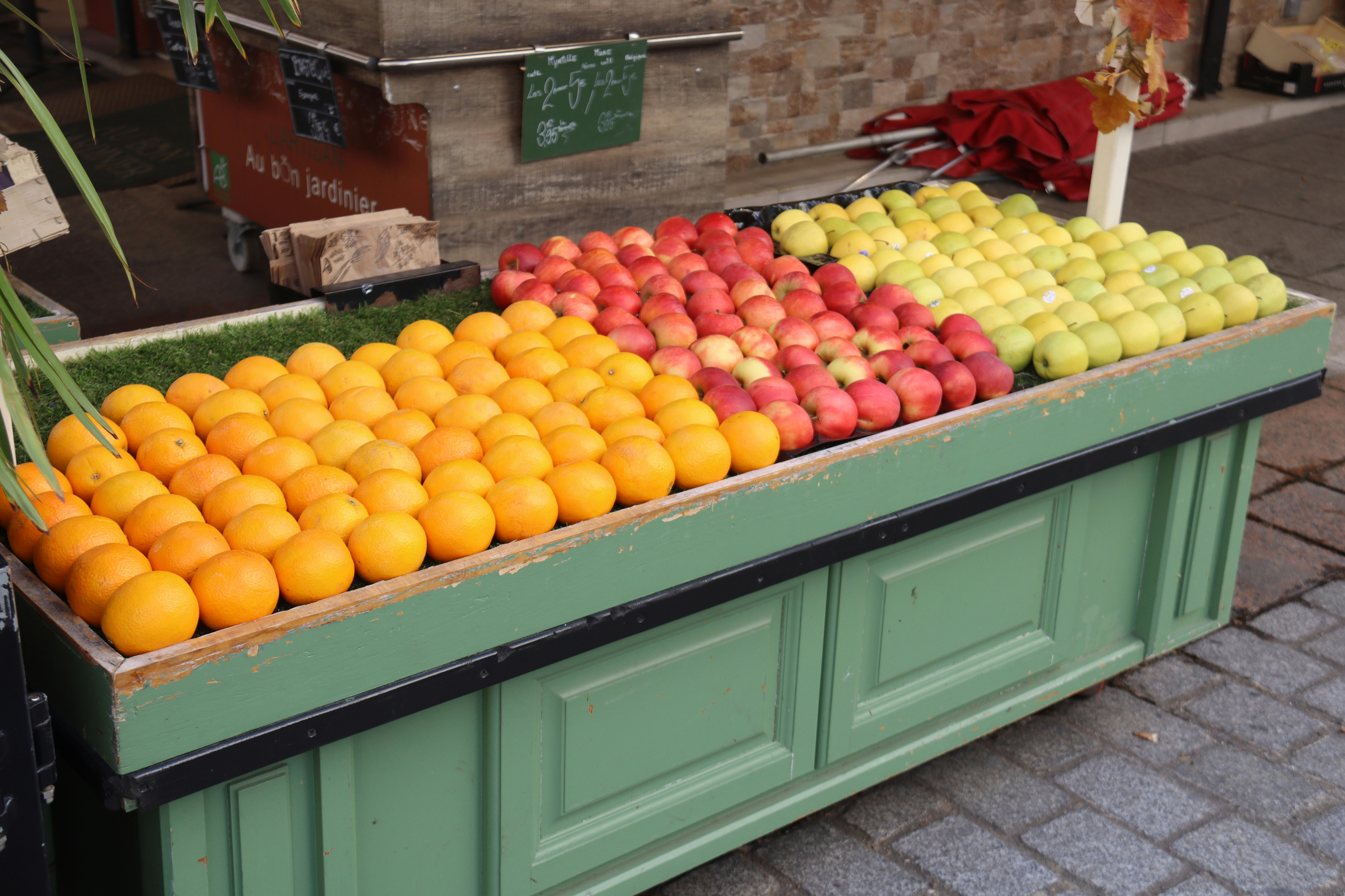 Oranges, apples, and lemons displayed on a green stand.
