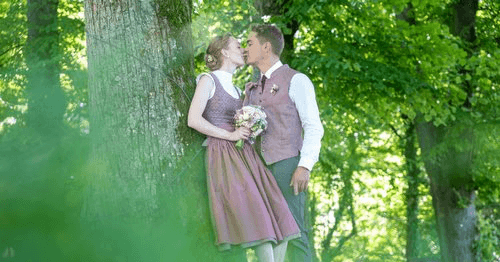 Bräutigam bindet der Braut im Dirndl erstmals die Schleife bei Hochzeit in Passau