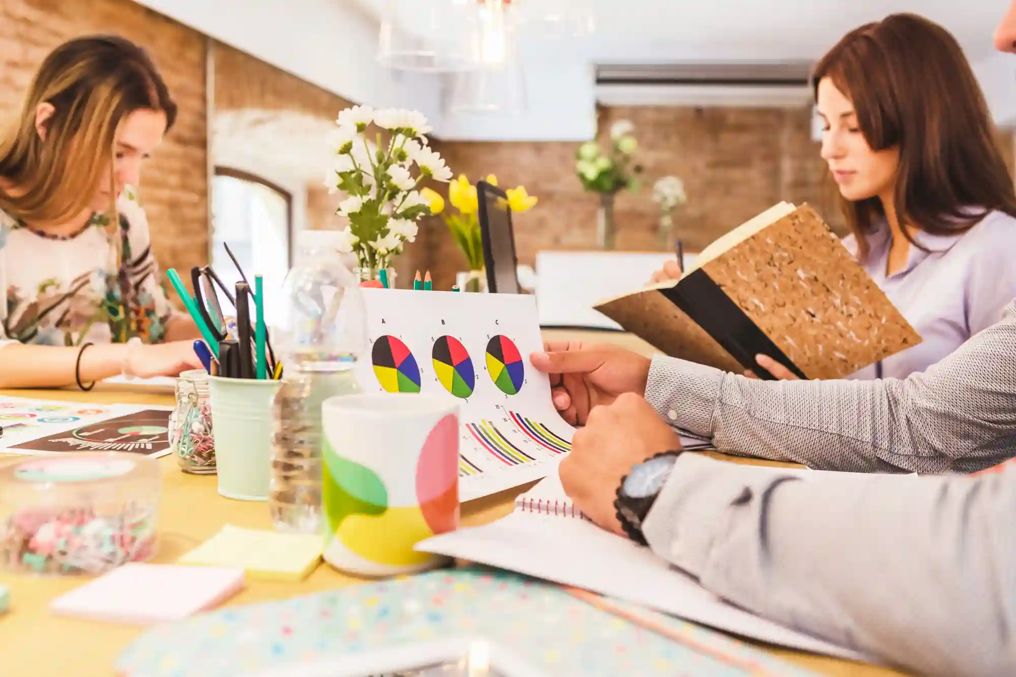 Image of three people collaborating on a project, reviewing a pie chart and taking notes in a modern office space.