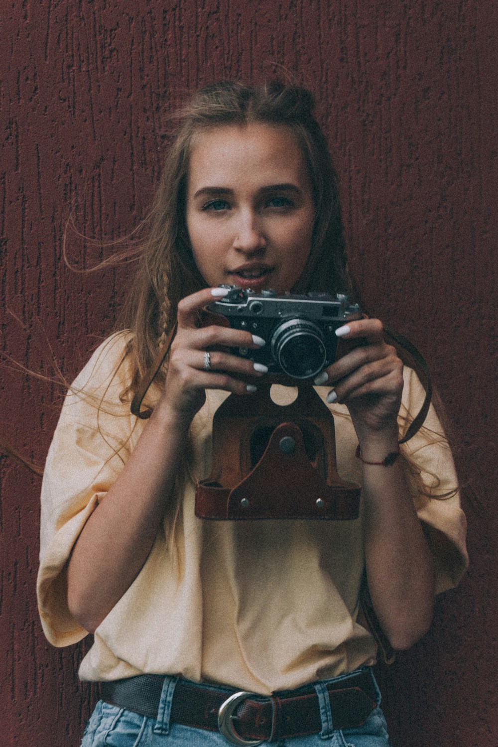A photographer in a cream T-shirt holding a vintage camera at chest height