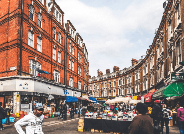 A smiling man with curly hair is sitting at a desk, looking at the camera, with a laptop and a lamp in the background.