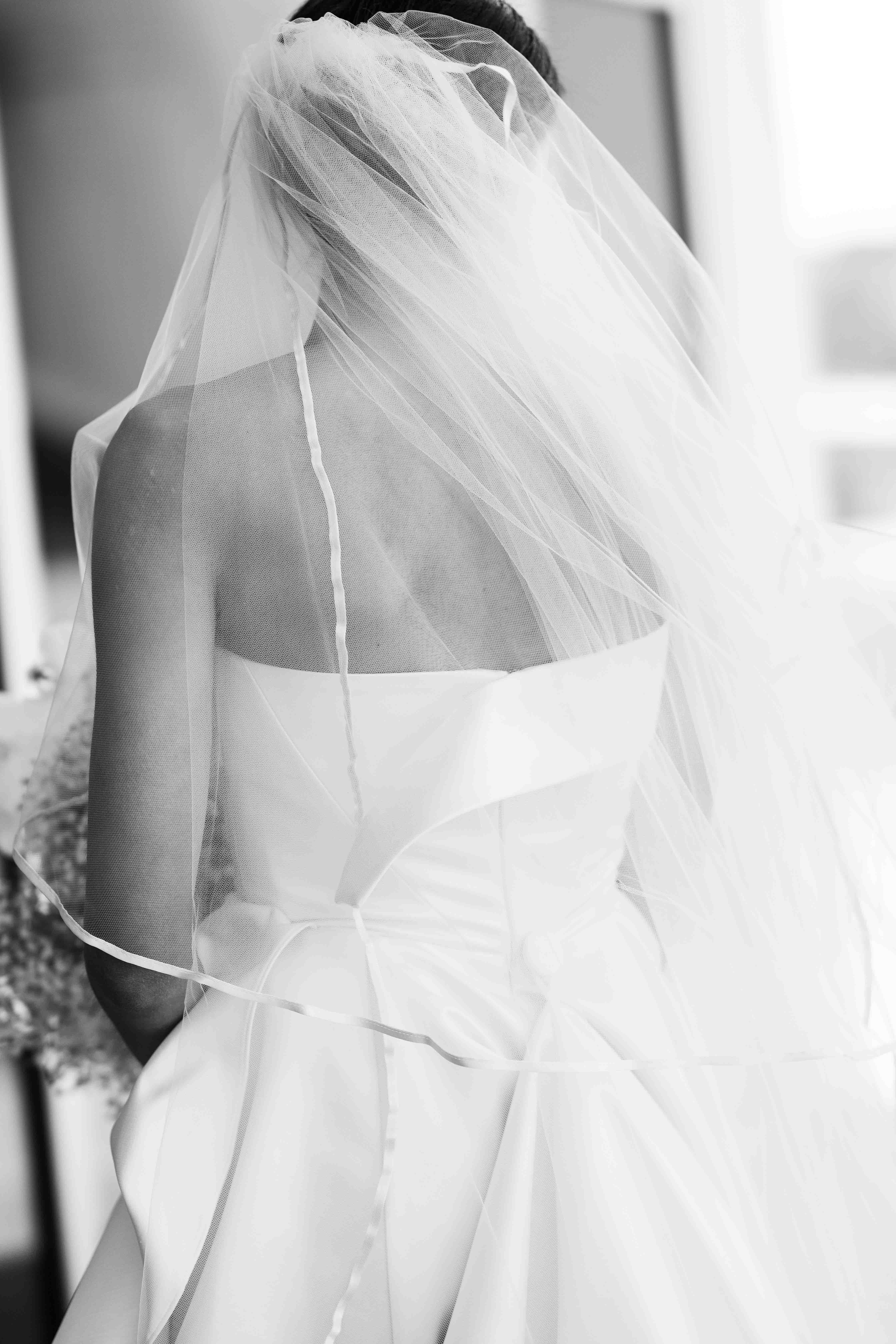 Black and white image of bride's back of dress and veil.