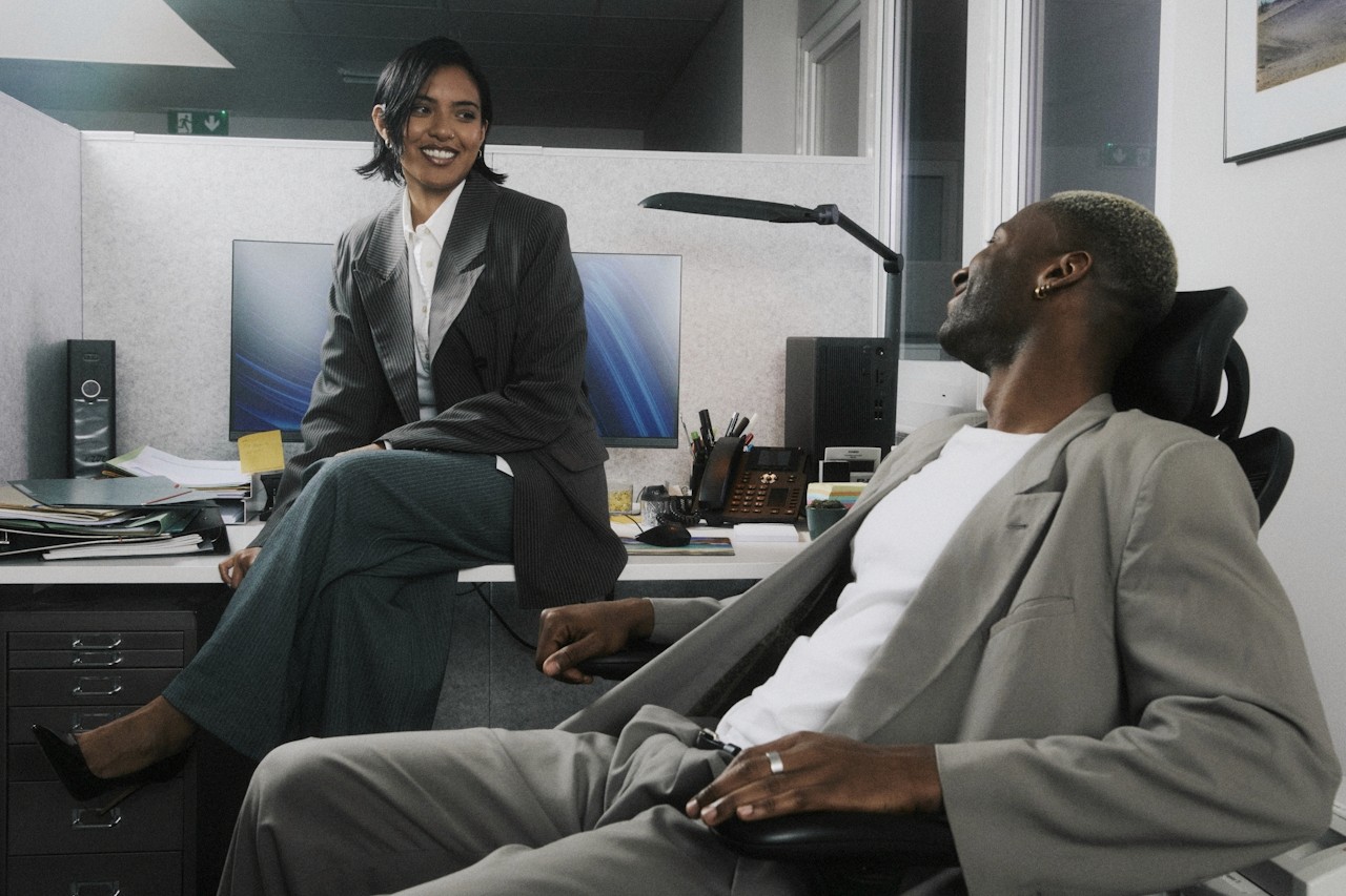Two colleagues having a relaxed conversation at their desks.