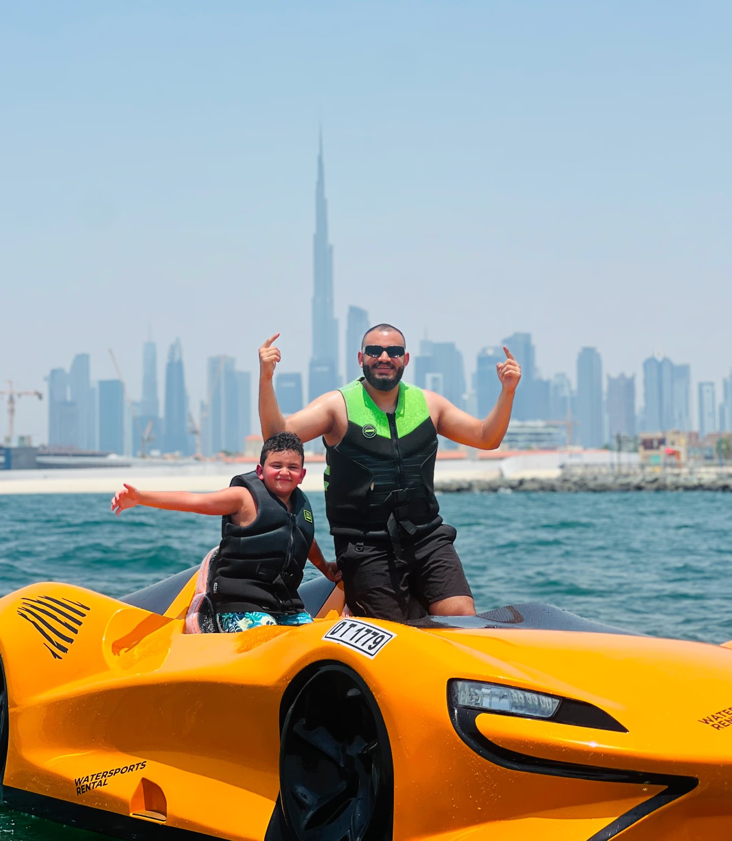 A father and son enjoying a ride in a bright orange jet car on the water with the Dubai skyline in the background