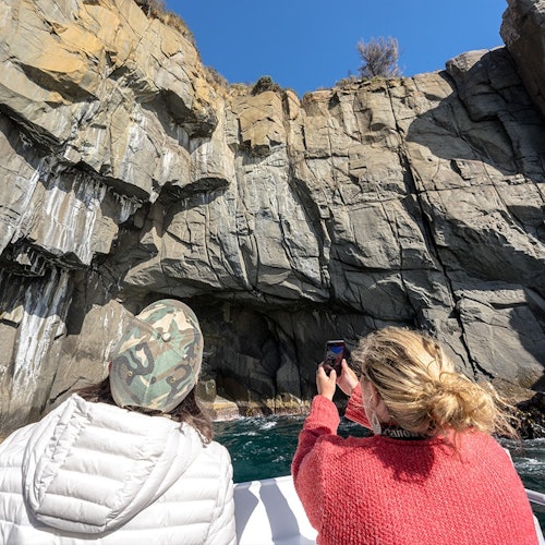 两个人在阳光明媚的日子里乘船拍摄了一张大岩壁的照片。