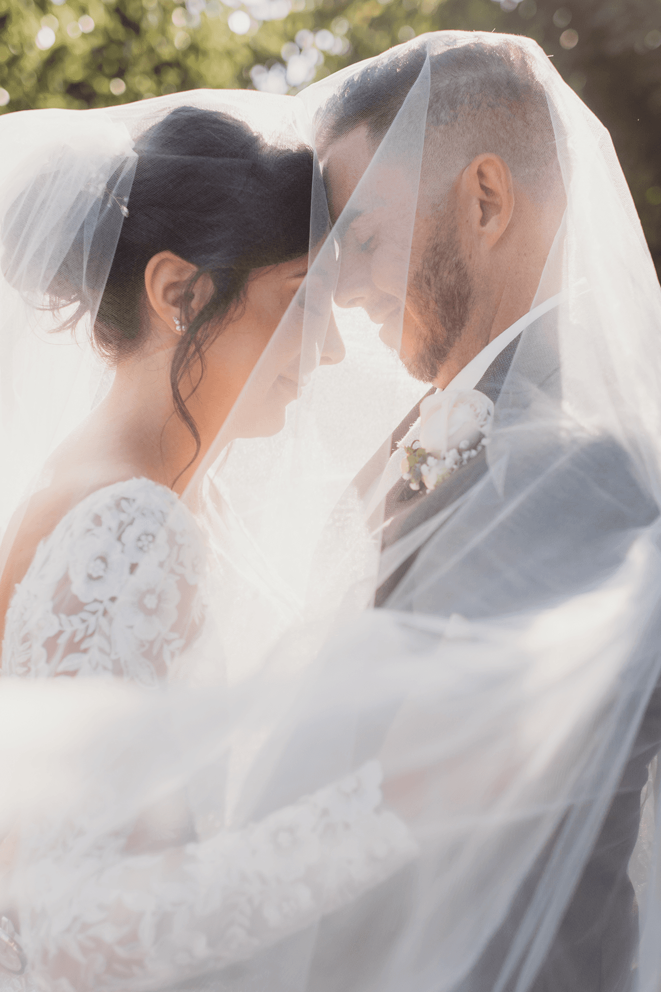 Bride and groom under the veil touching foreheads and smiling