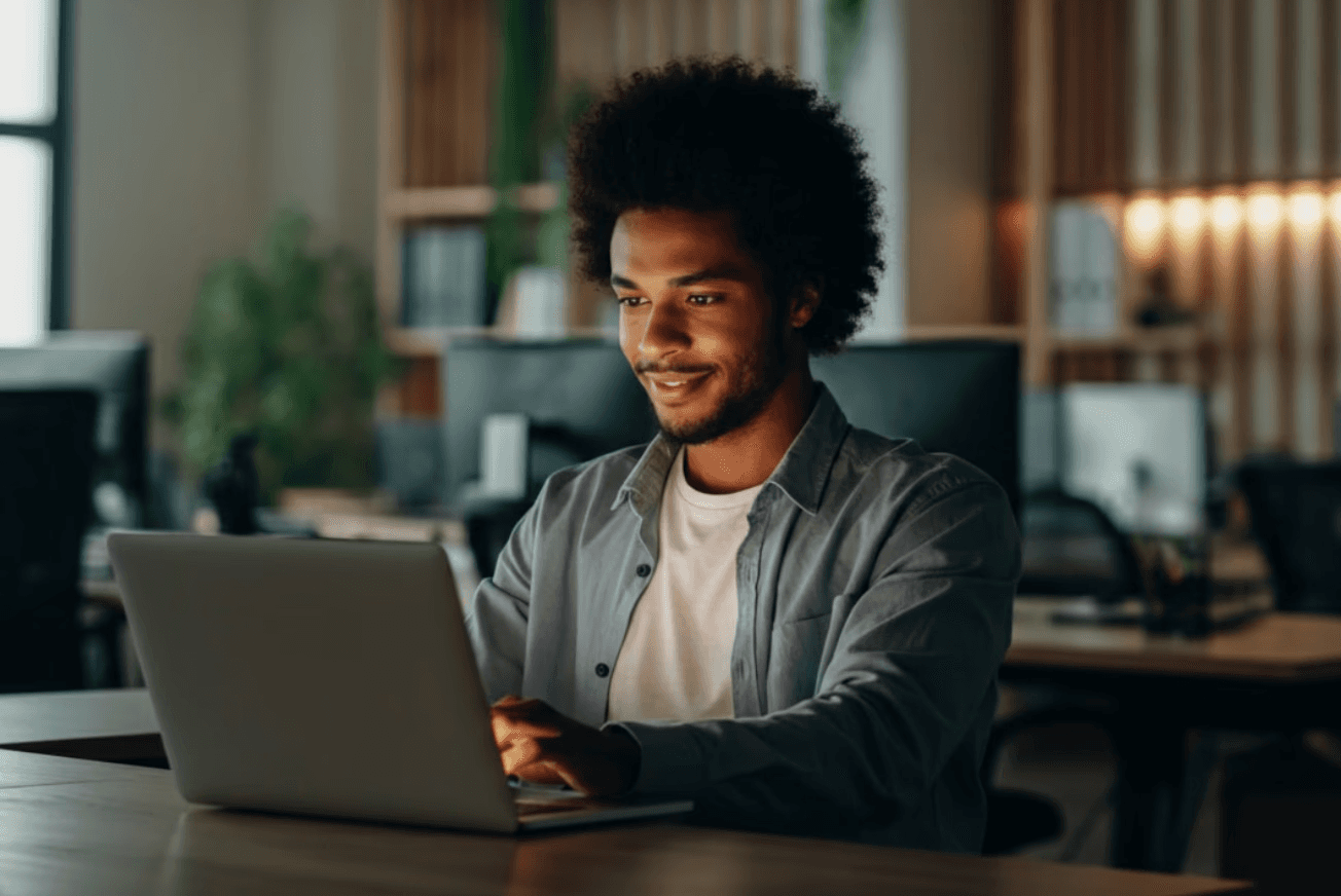 A talent recruiter with a soft smile working on her laptop in the office. The angle is on her face so we can't see what's is on the screen. She is wearing a blazer 