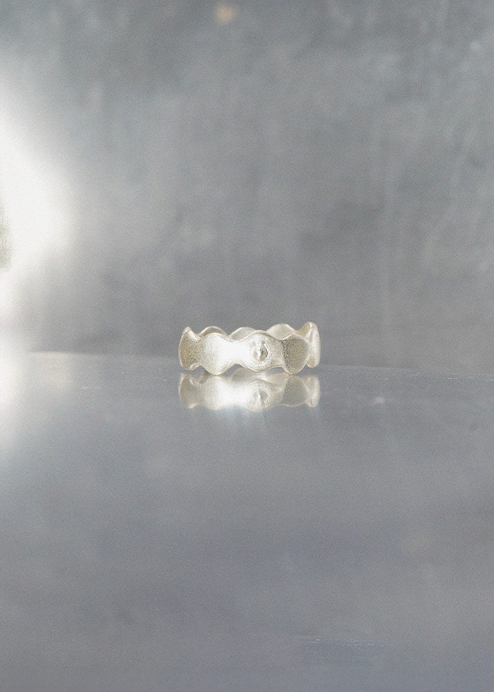 Silver ring with wavy design on a reflective gray surface