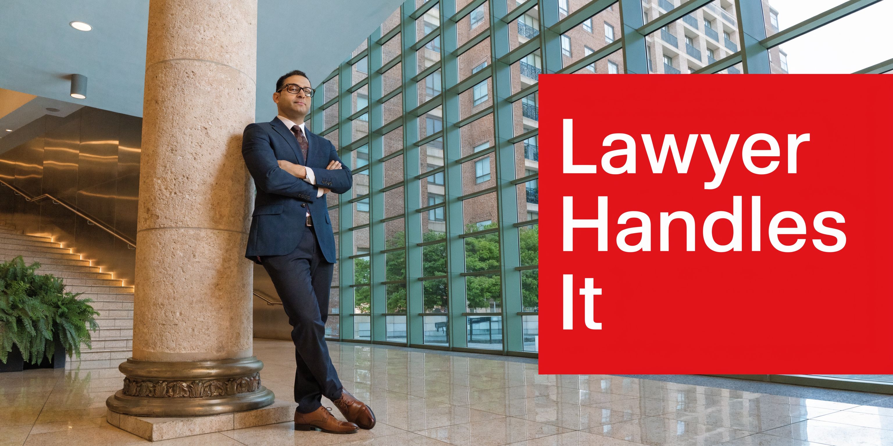 A professional lawyer wearing a suit stands leaning against a stone pillar in a modern office building lobby.