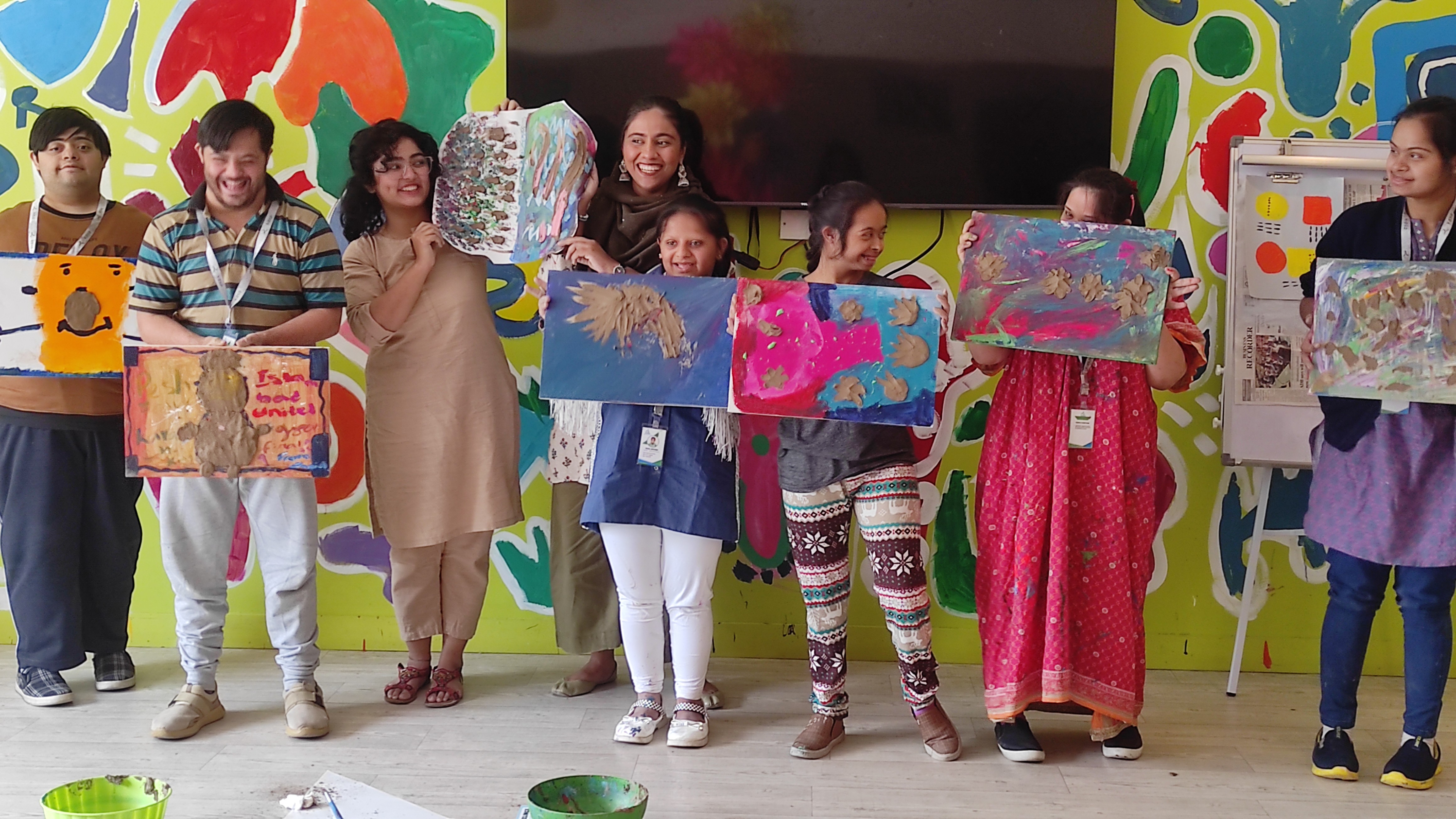 A group of children with down syndrome holding their artworks alongside two facilitators