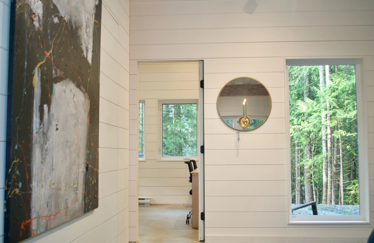 Modern two-story home with large glass windows, warmly lit interiors, and a balcony. Surrounded by trees and a manicured lawn at dusk. Cozy ambiance.