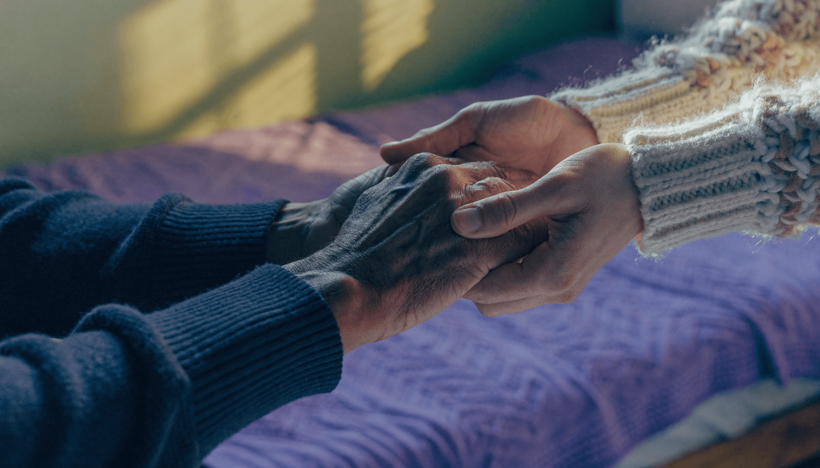 A cinematic, hyper-realistic 8k photograph of a pair of hands gently holding another person's hand in a warm, sunlit room.