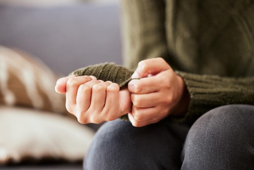 A close up image of a person in a green jumper in counselling, clutching their sleeves 