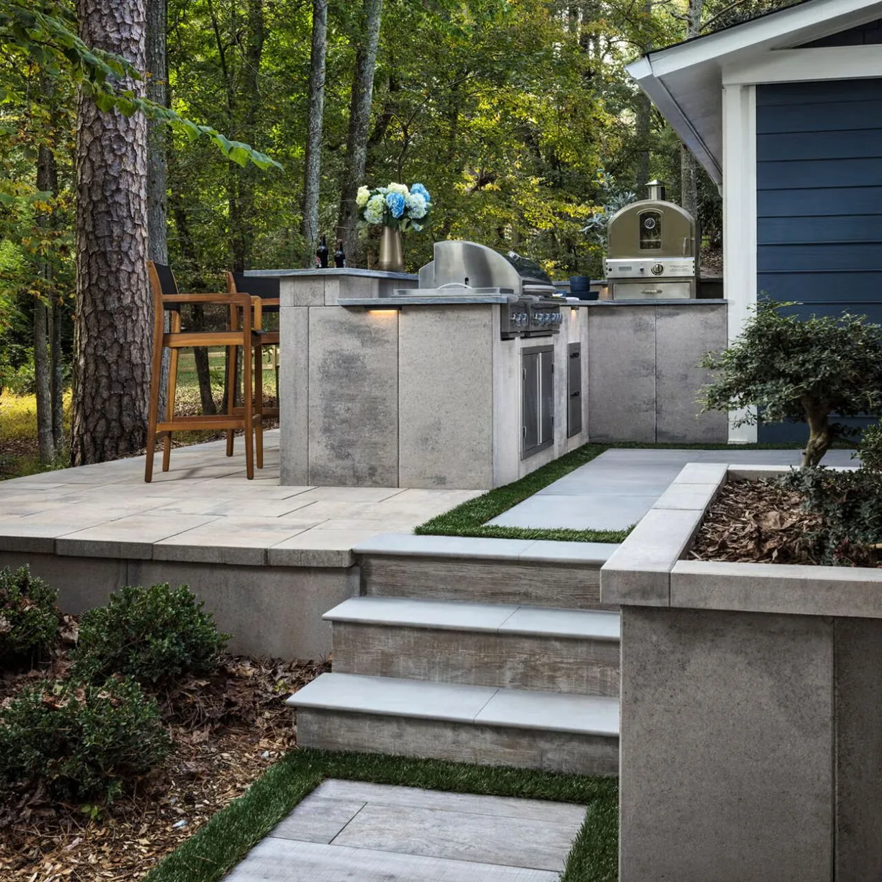 Steps between spaces Broad garden steps connecting rectangular paving and an outdoor cooking area beside a house.