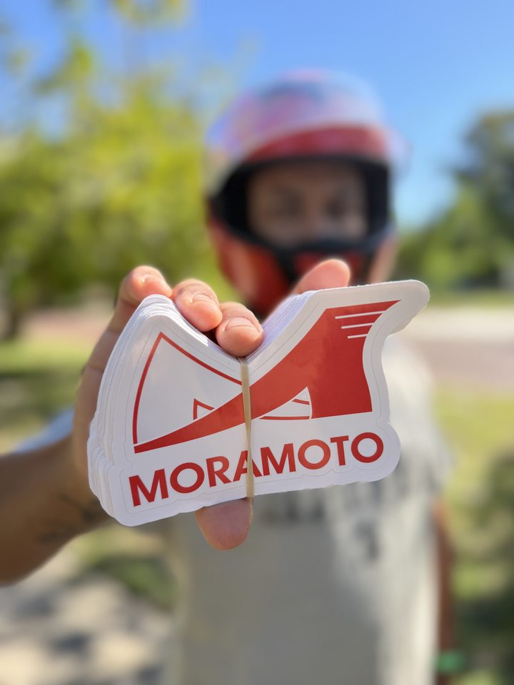 A person holding a stack of red and white Moramoto stickers with shaped outlines.