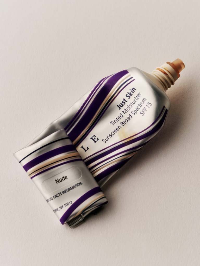 A tube of tinted moisturizer and sunscreen labeled 'Just Skin' in a 'Nude' shade, featuring purple and silver packaging.