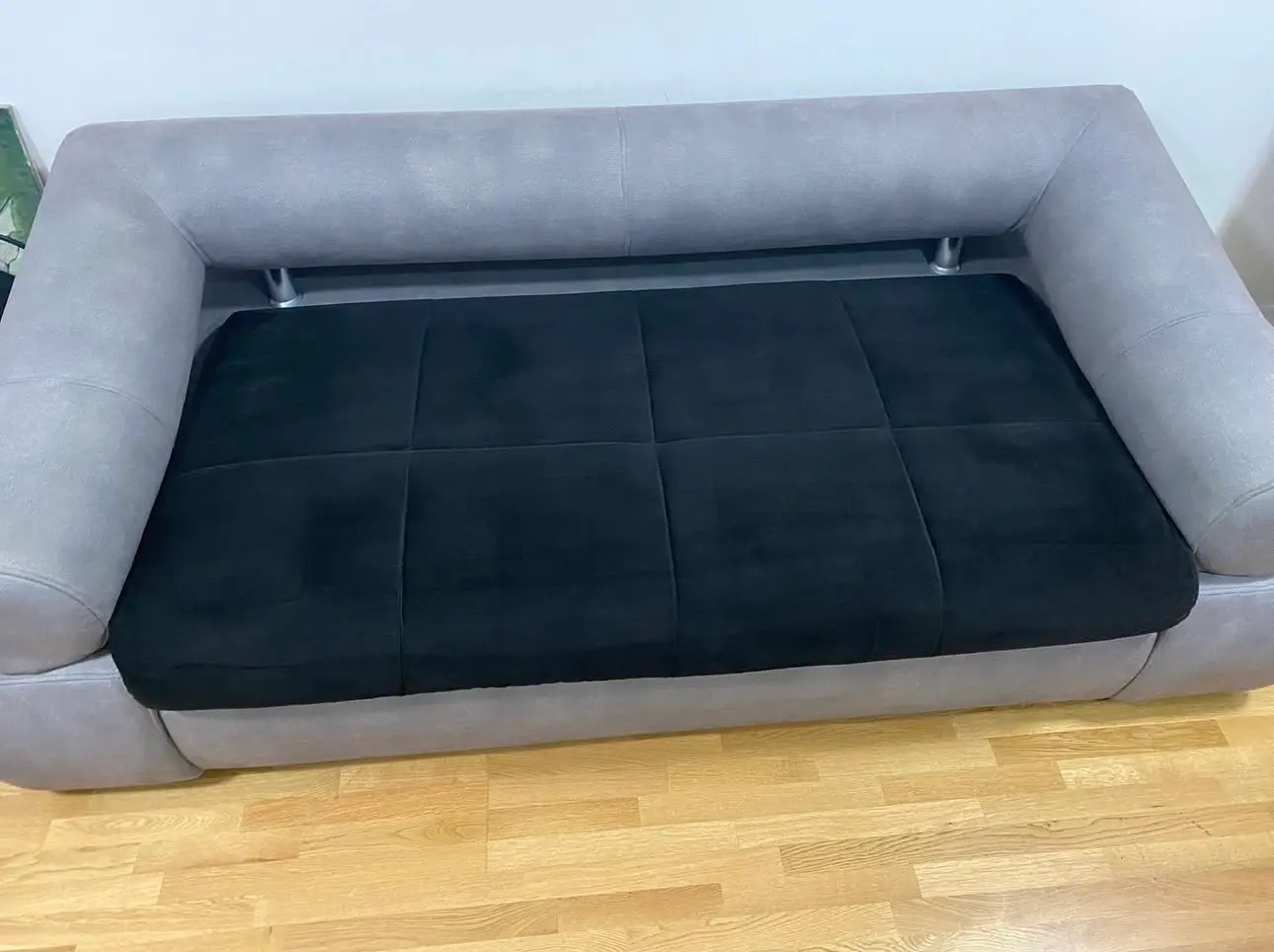 Deeply cleaned grey and black fabric sofa with vacuumed cushions and sanitized upholstery on a hardwood floor.
