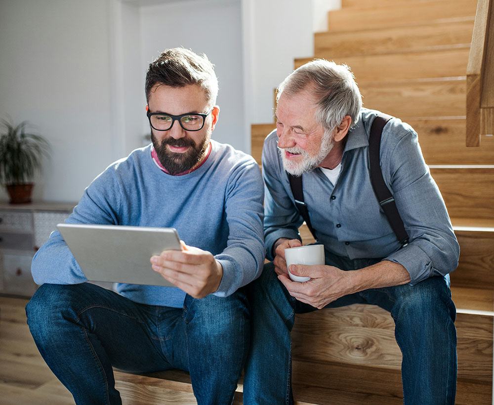 Two men sitting on a staircase, one holding a tablet and the other holding a coffee mug.