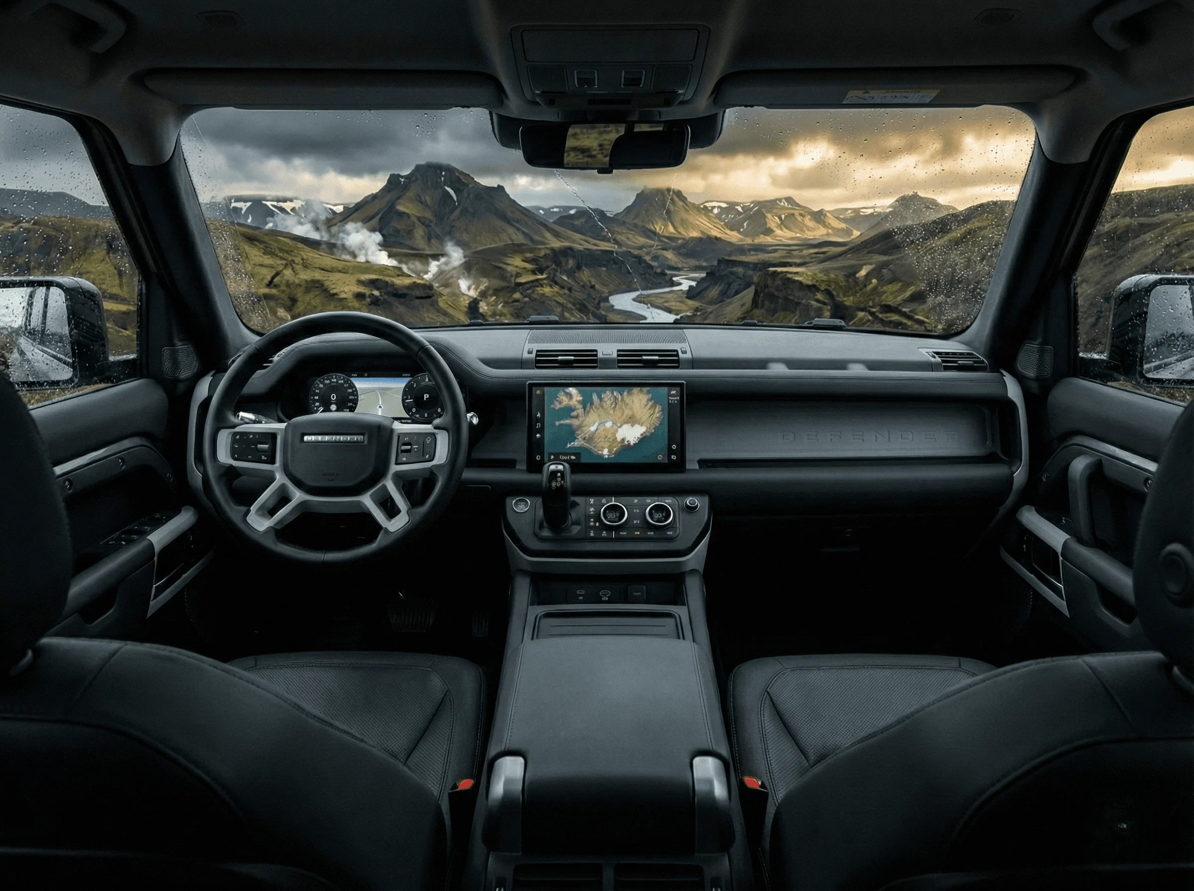 View from the driver's seat of a Land Rover Defender looking out through the windshield at a mountainous landscape.