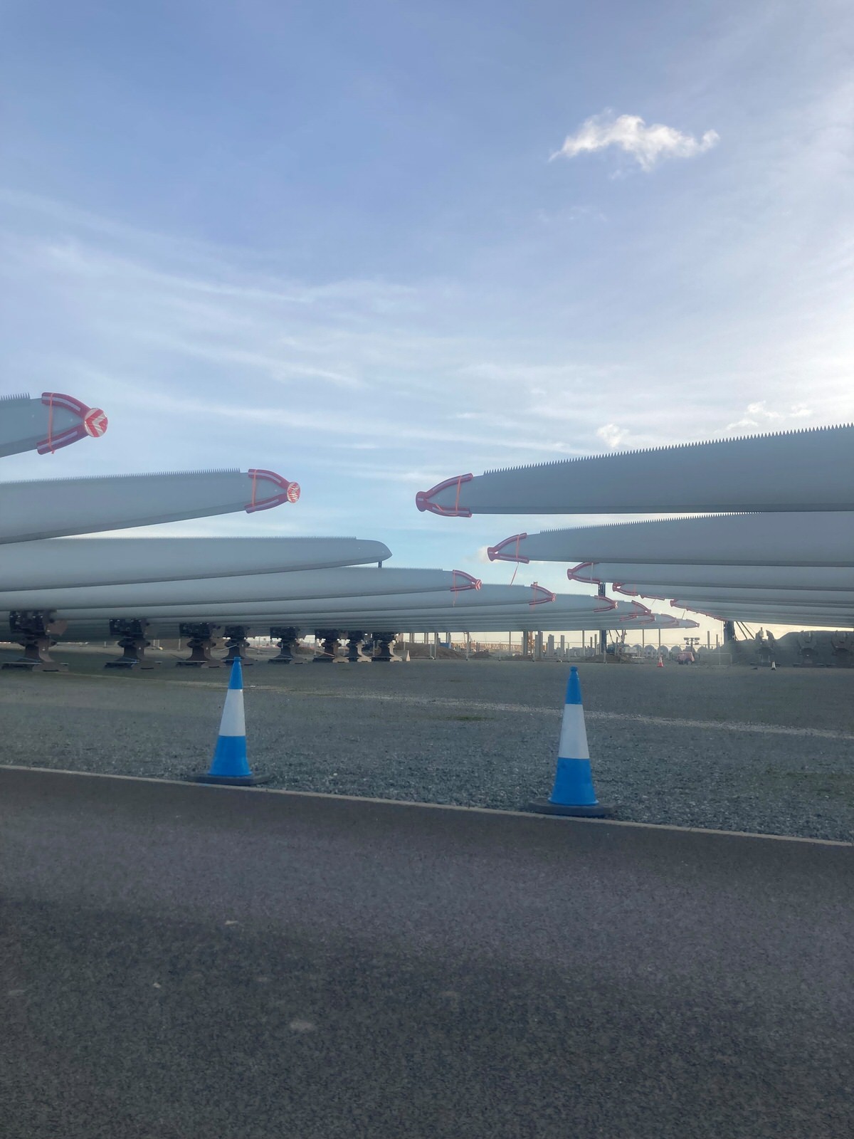 Wind turbine blades stored horizontally on transport supports at an industrial site