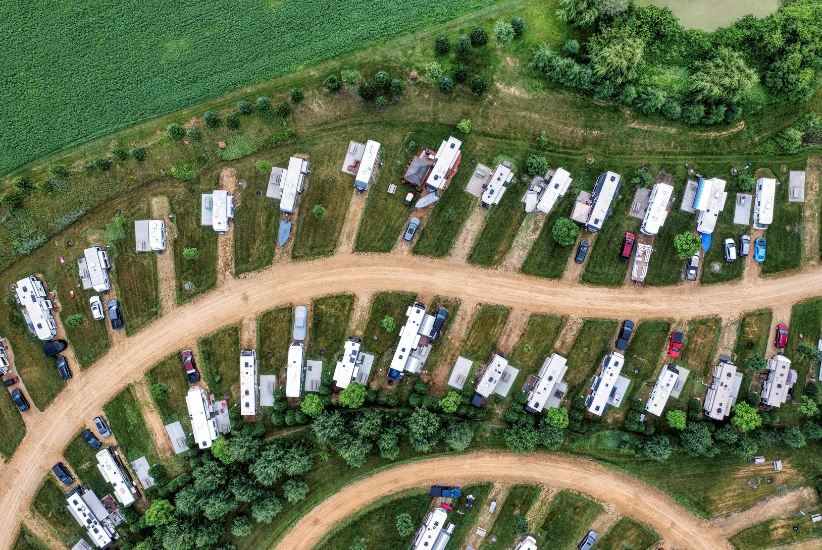 Aerial drone view of a full RV park with multiple campers and trailers parked in organized rows alongside trees.