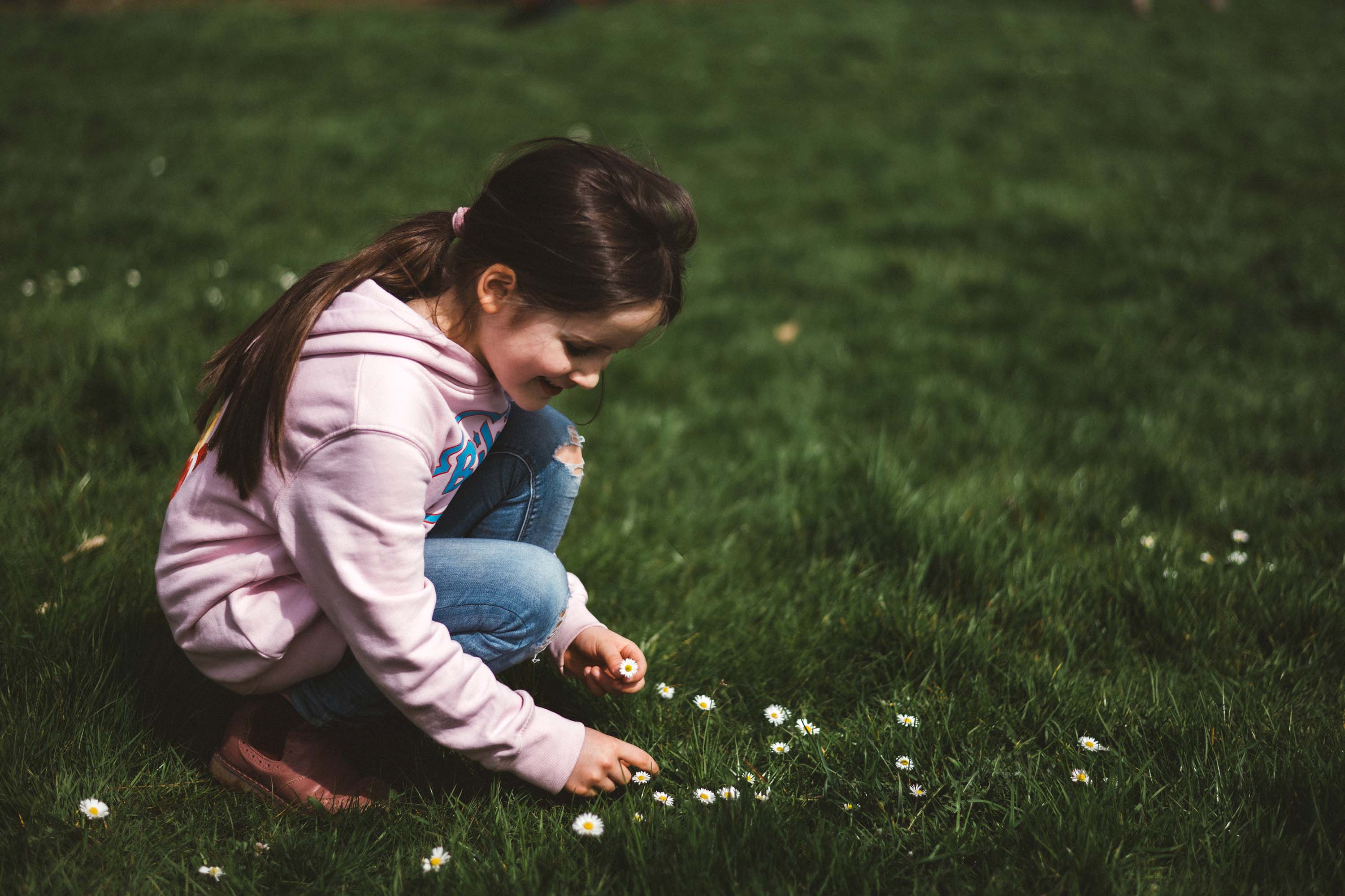 Authentische Kindergartenfotografie Gevelsberg: Ein Mädchen in einem rosafarbenen Pullover lacht glücklich beim Klettern auf einem Holzgerüst. Professionelles Outdoor-Porträt mit weichem Bokeh von PK photography 4 Kids NRW.