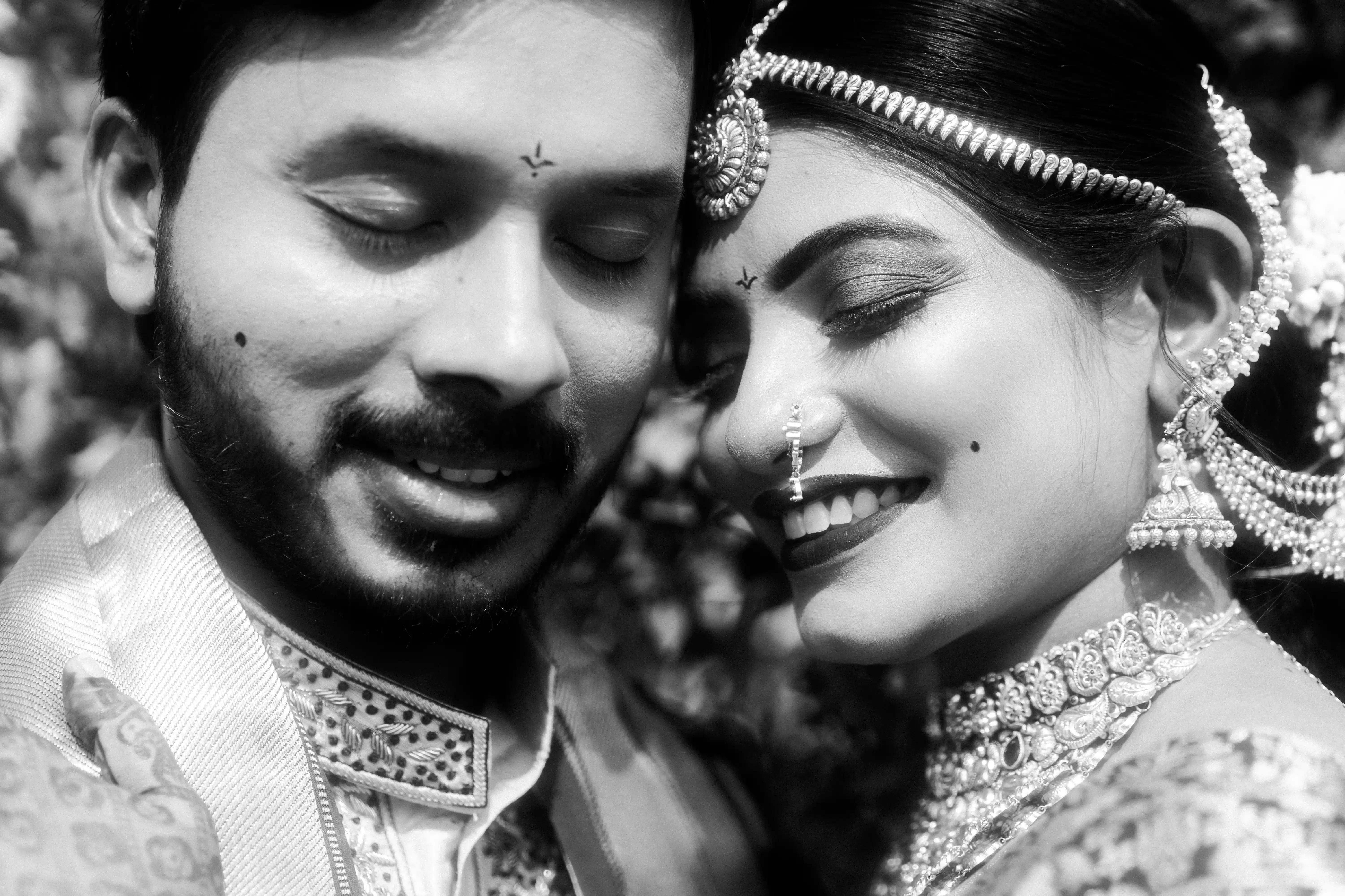 Intimate black-and-white portrait of a bride and groom sharing a joyful moment, highlighting their serene expressions and traditional jewelry, crafted by Out of The Blues Fine Art Wedding Photography in Hyderabad.