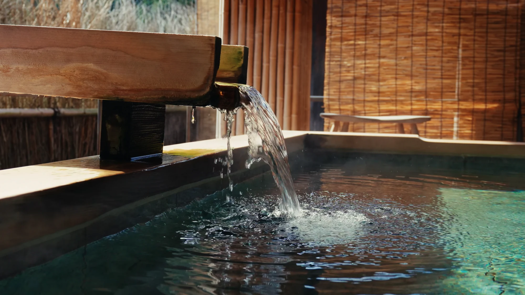 Hot spring water running from a timber spout into a small private bath.